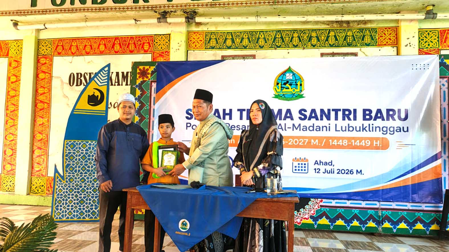 Pimpinan Ponpes Al Madani Lubuk Linggau Ustadz Moh Arpan Haj didampingi Pengasuh Keputrian Ummi Erma Yunita, menyerahkan secara simbolis perlengkapan belajar kepada salah satu santri baru MTs Al Madani. Foto : Yezi Fadly / Linggau Pos