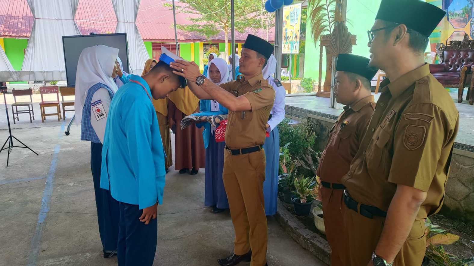 Kepala SMAN Purwodadi, Agus Salim memasang perlengkapan MPLS kepada perwakilan siswa baru, didampingi Ketua Pelaksana MPLS, Indramaya pada acara pembukaan MPLS, Senin 13 Juli 2026. Foto : SMAN Purwodadi