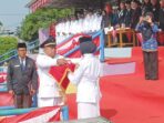 Camat Tugumulyo P Sujatmiko., S.Si., M.Pd, menyerahkan benderah Merah Putih kepada Pembawa Baki saat upacara bendera Peringatan HUT ke 81 Kemerdekaan Republik Indonesia Tahun 2026, tingkat Kecamatan Tugumulyo, Senin 17 Agustus 2026. Sumber Foto : MUSLIMIN