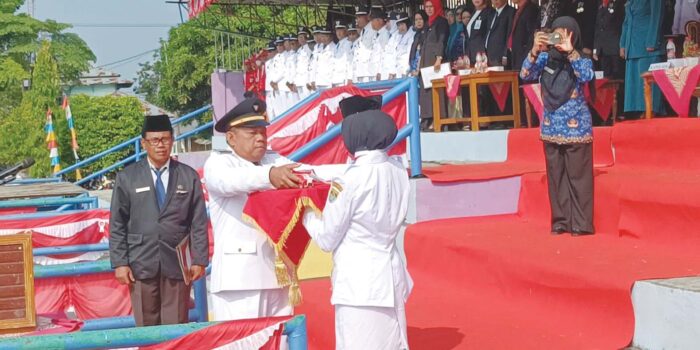 Camat Tugumulyo P Sujatmiko., S.Si., M.Pd, menyerahkan benderah Merah Putih kepada Pembawa Baki saat upacara bendera Peringatan HUT ke 81 Kemerdekaan Republik Indonesia Tahun 2026, tingkat Kecamatan Tugumulyo, Senin 17 Agustus 2026. Sumber Foto : MUSLIMIN