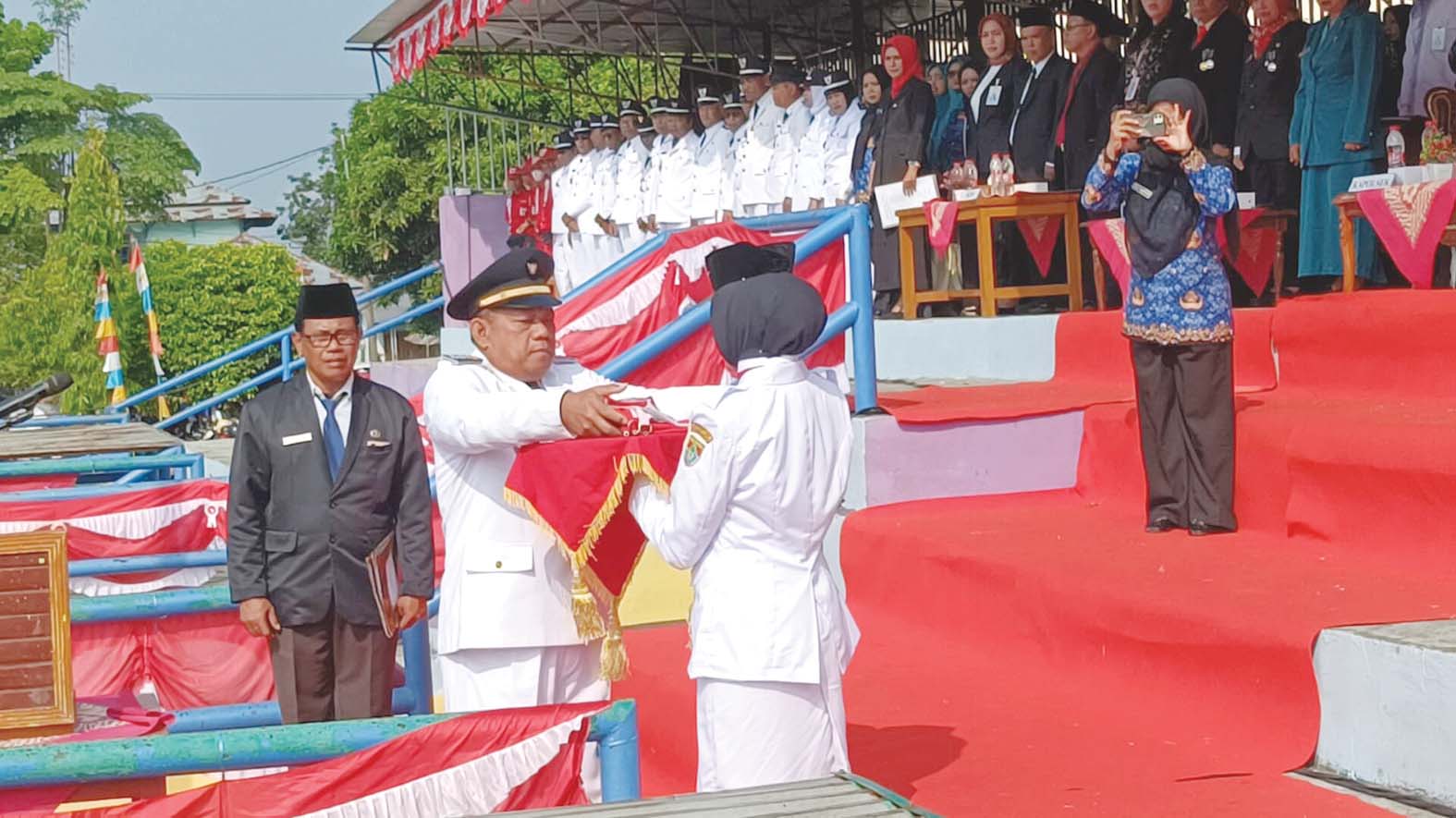 Camat Tugumulyo P Sujatmiko., S.Si., M.Pd, menyerahkan benderah Merah Putih kepada Pembawa Baki saat upacara bendera Peringatan HUT ke 81 Kemerdekaan Republik Indonesia Tahun 2026, tingkat Kecamatan Tugumulyo, Senin 17 Agustus 2026. Sumber Foto : MUSLIMIN